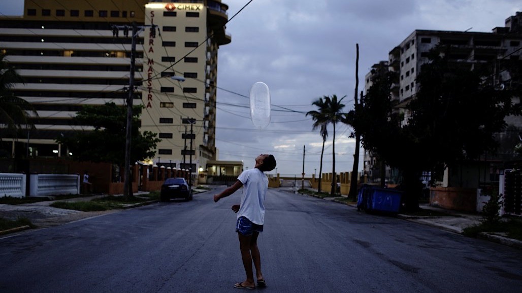 Un joven juega con un condón como globo en La Habana. Al fondo, sede del CIMEX, corporación de los militares cubanos.