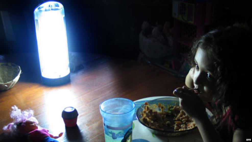 Una niña come a la luz de una lámpara.