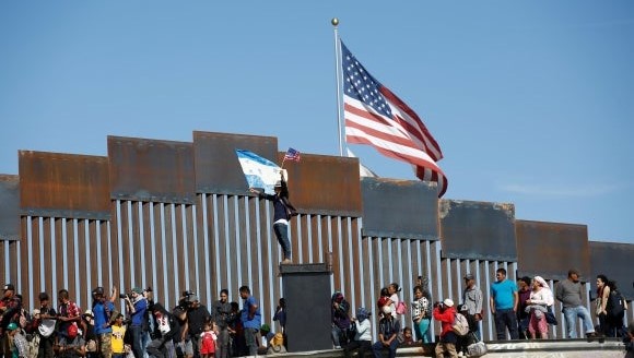 Emigrantes ante el muro fronterizo de EEUU.