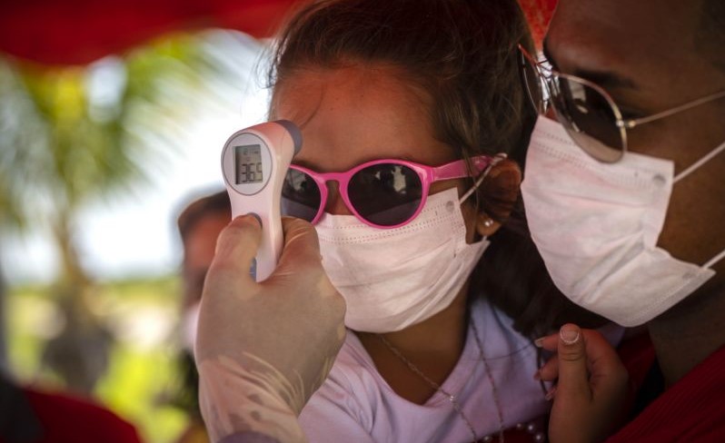 A una niña con mascarilla le toman la temperatura en un puesto de control en la entrada de La Habana.