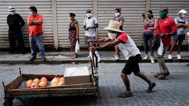 Un hombre pasa con una carretilla frente a una cola en Cuba.