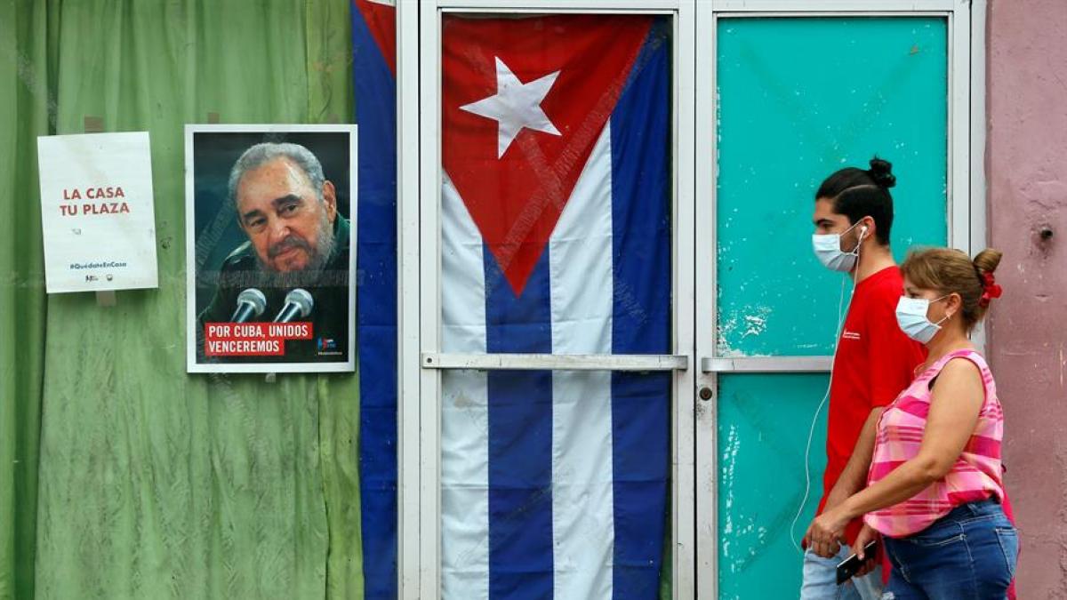 Dos cubanos caminan con mascarillas sanitarias por la calle en Cuba. 