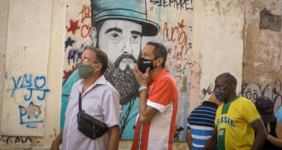 Cubanos tras un cartel con la imagen de Fidel Castro.
