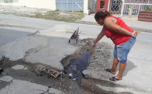 Una mujer en Santiago de Cuba señala un salidero sin solucionar en la calle.