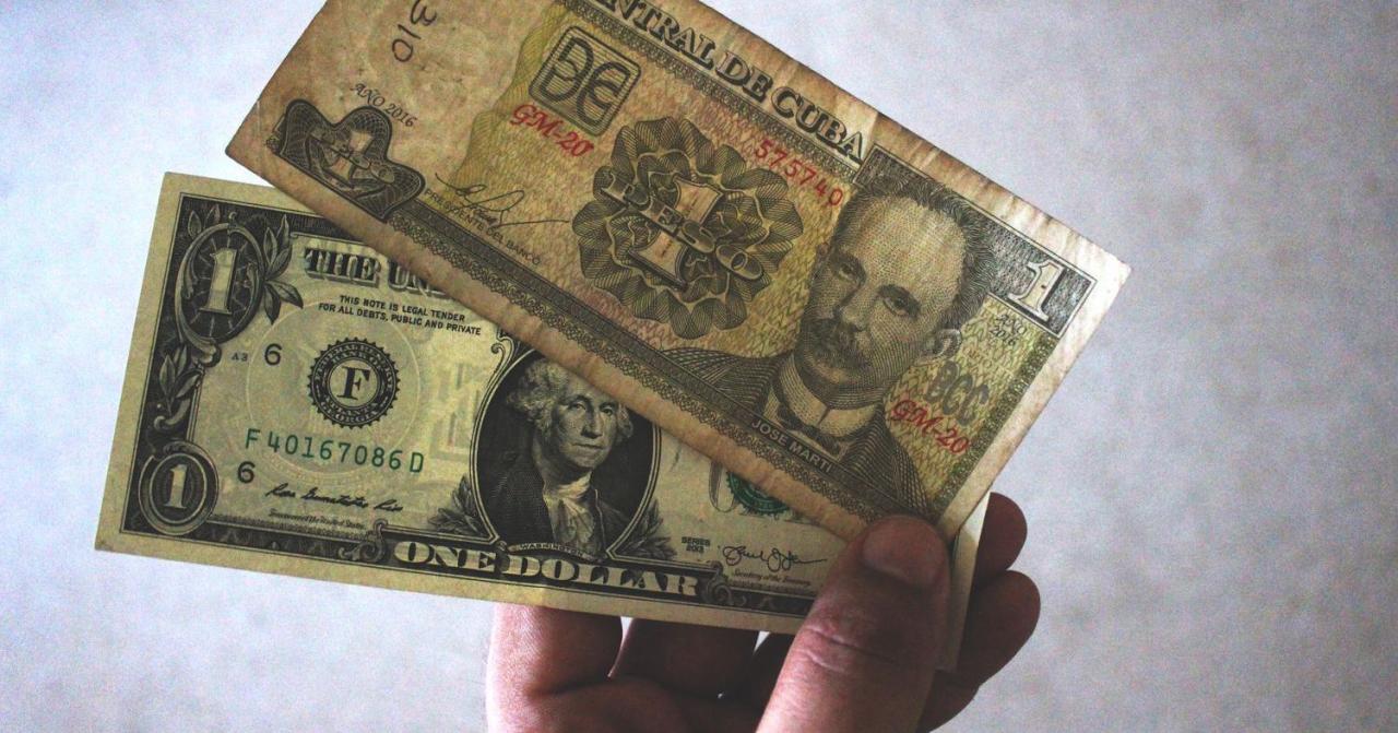 Una persona sostiene un peso cubano y un dólar.