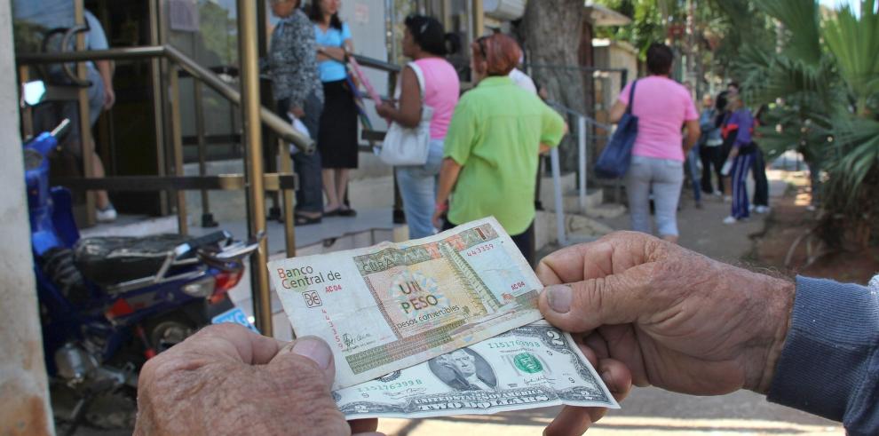 Un hombre muestra un peso convertible cubano y dos dólares estadounidenses.