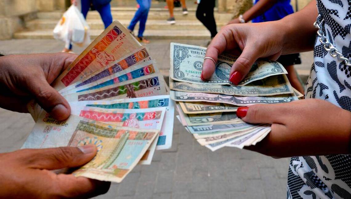 Dos personas sostienen billetes de pesos cubanos convertibles y dólares estadounidenses.