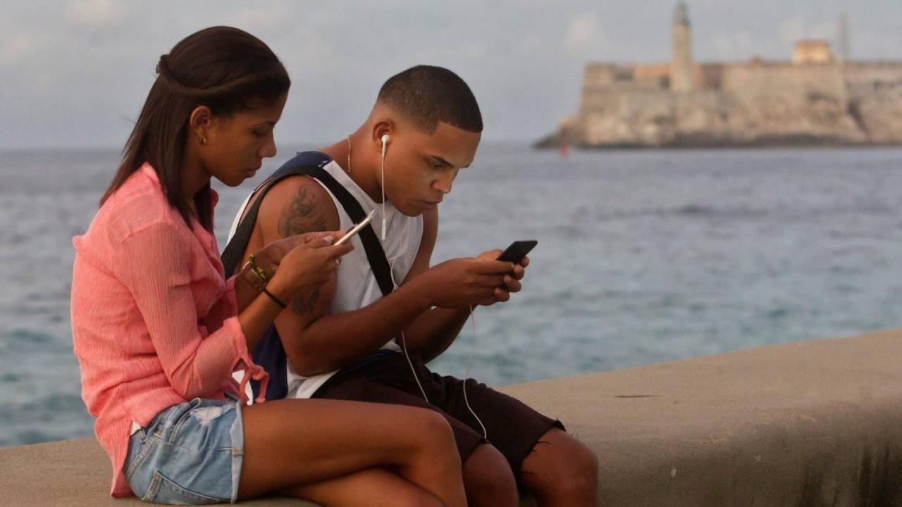 Jóvenes cubanos conectados a través de sus celulares en el Malecón de La Habana.