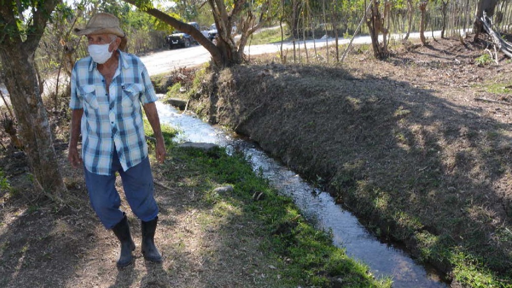 Un campesino camina junto a un salidero de agua convertido en zanja.