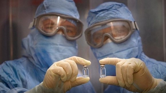 Científicos cubanos sostienen frascos de vacunas.