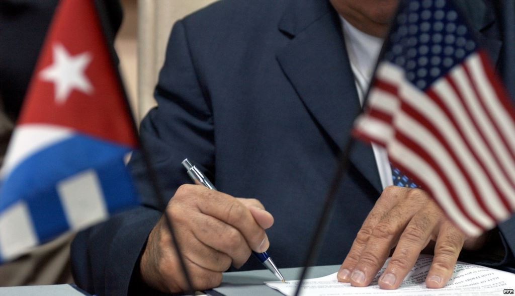 Un funcionario firma un documento ante las banderas de Cuba y EEUU.