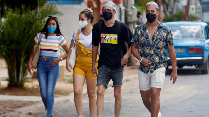 Jóvenes cubanos caminan por la calle con mascarillas.