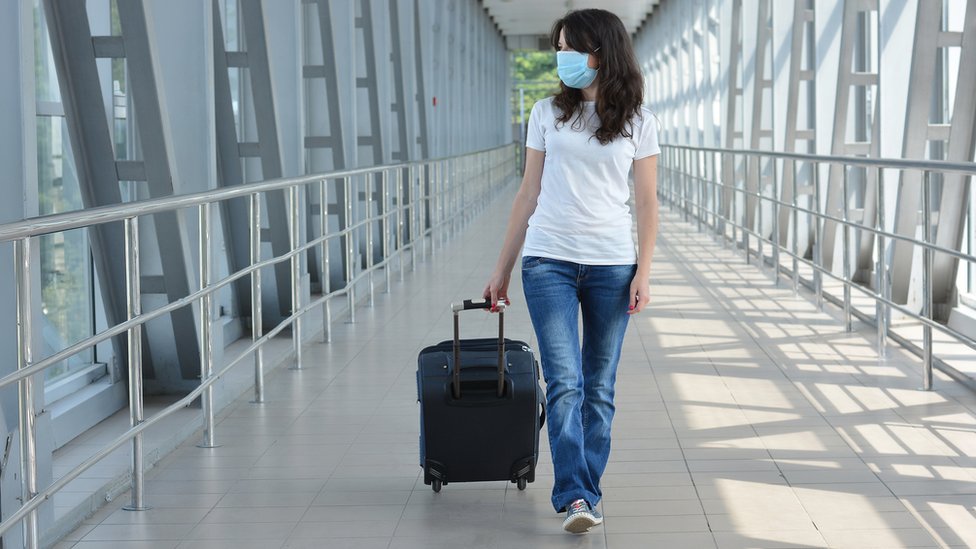 Una mujer con mascarilla recorre un pasillo en un aeropuerto.