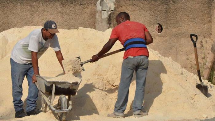 Dos hombres cargan arena para la construcción en una carretilla.