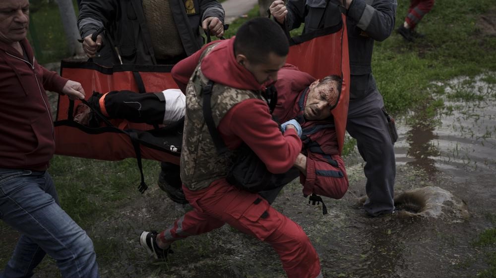 Residentes ayudan a un trabajador de emergencia a llevar a un hombre a una ambulancia luego de un bombardeo ruso en Járkov, Ucrania, 27 de abril de 2022.