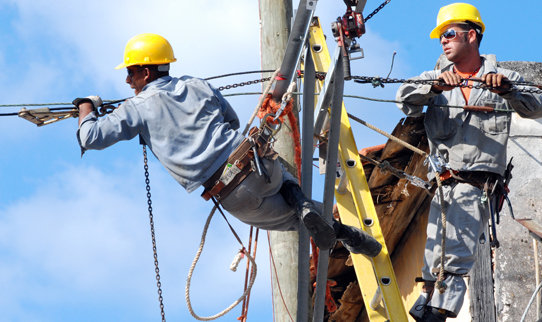 Dos trabajadores reparan líneas eléctricas en Cuba.