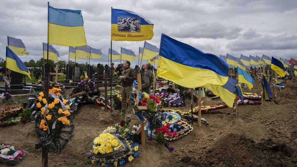 Dos soldados de la guardia nacional beben un trago en memoria de dos soldados fallecidos, en el cementerio de Jarkov, este de Ucrania, domingo 22 de mayo.