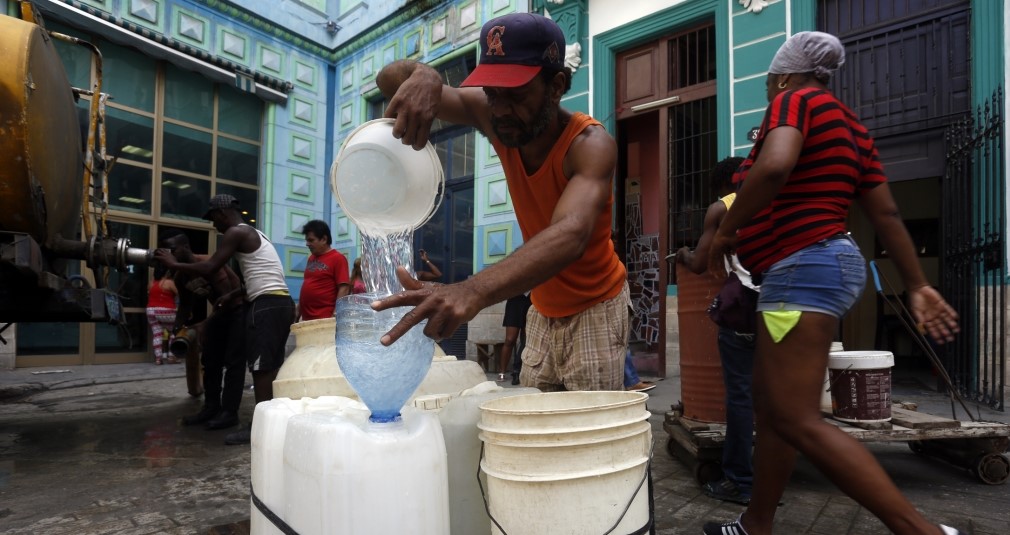 Cubanos llenan vasijas con una pipa de agua.