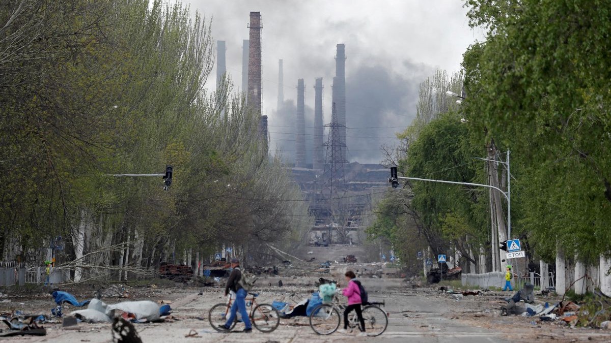Personas cruzan la calle mientras el humo se eleva sobre una planta de Azovstal en Mariupol, Ucrania, el 2 de mayo de 2022.
