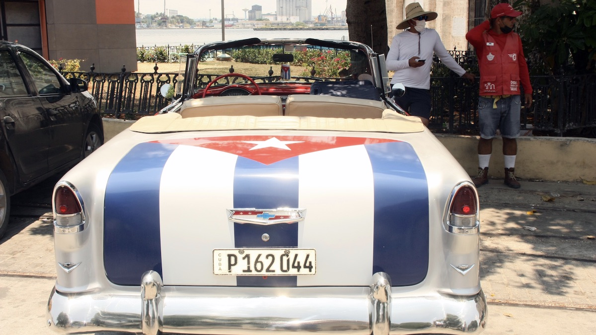 Dos cubanos junto a un auto de alquiler para turistas.