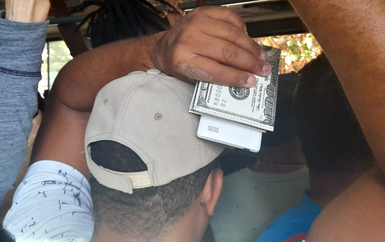 Un hombre con su teléfono y su billetera en la mano en una guagua de La Habana.