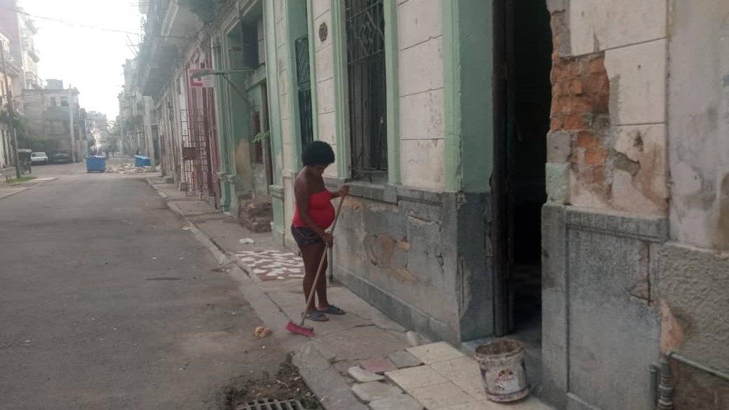 Una mujer embarazada barre el frente de su vivienda en La Habana.