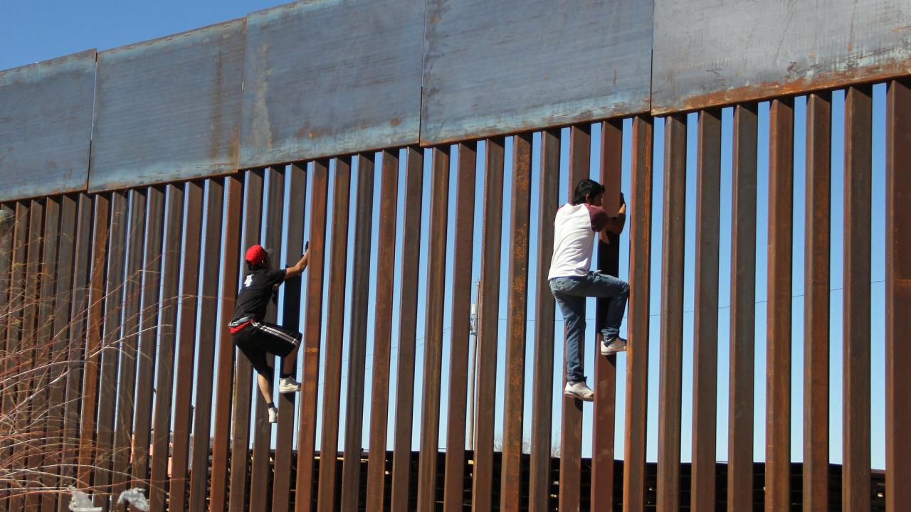 Migrantes escalando el muro fronterizo entre México y EEUU.