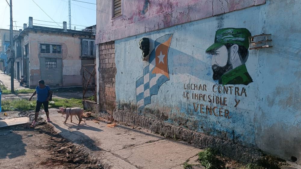 A woman dodges potholes on a Havana street graced with regime propaganda.