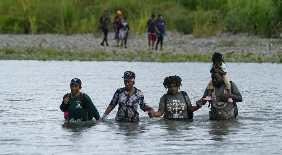 Migrantes haitianos vadean el río Tuquesa después de caminar por el Tapón del Darién en Panamá.