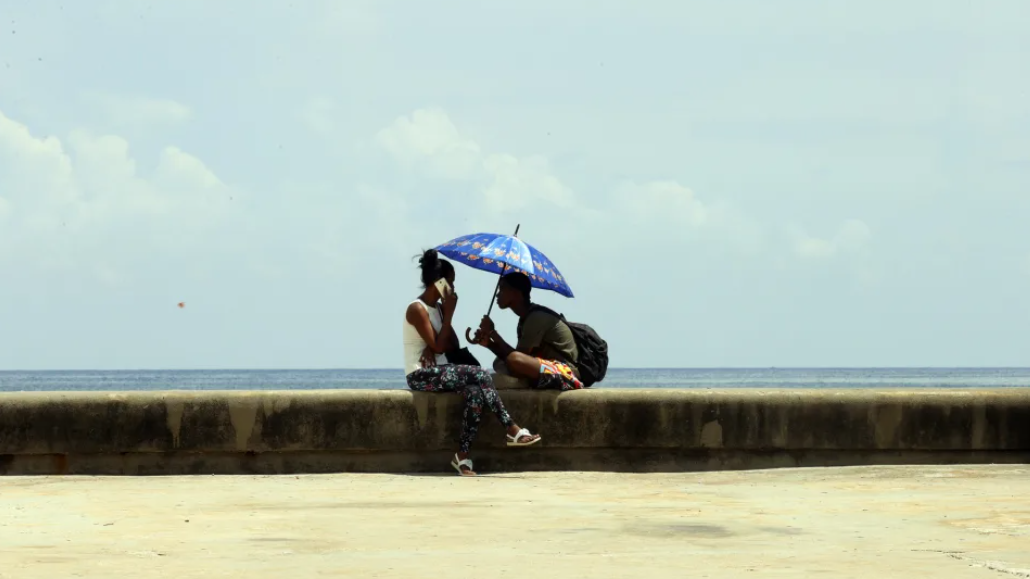 Dos cubanos se protegen del sol en el Malecón de La Habana.