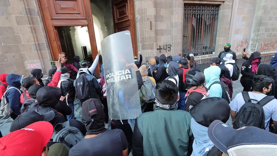 Jóvenes mexicanos rompen una puerta del Palacio Nacional, con AMLO en el edificio.