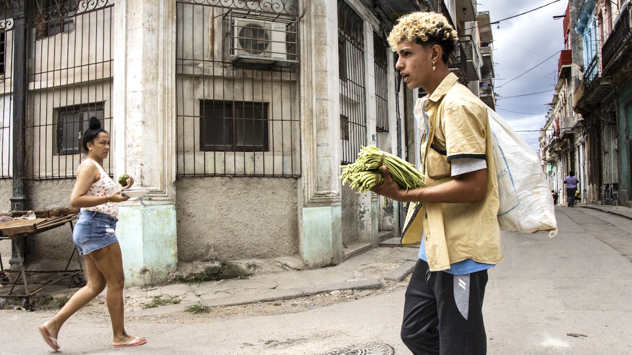 Una mujer con un aguacate y un joven con un mazo de habichuelas en La Habana.