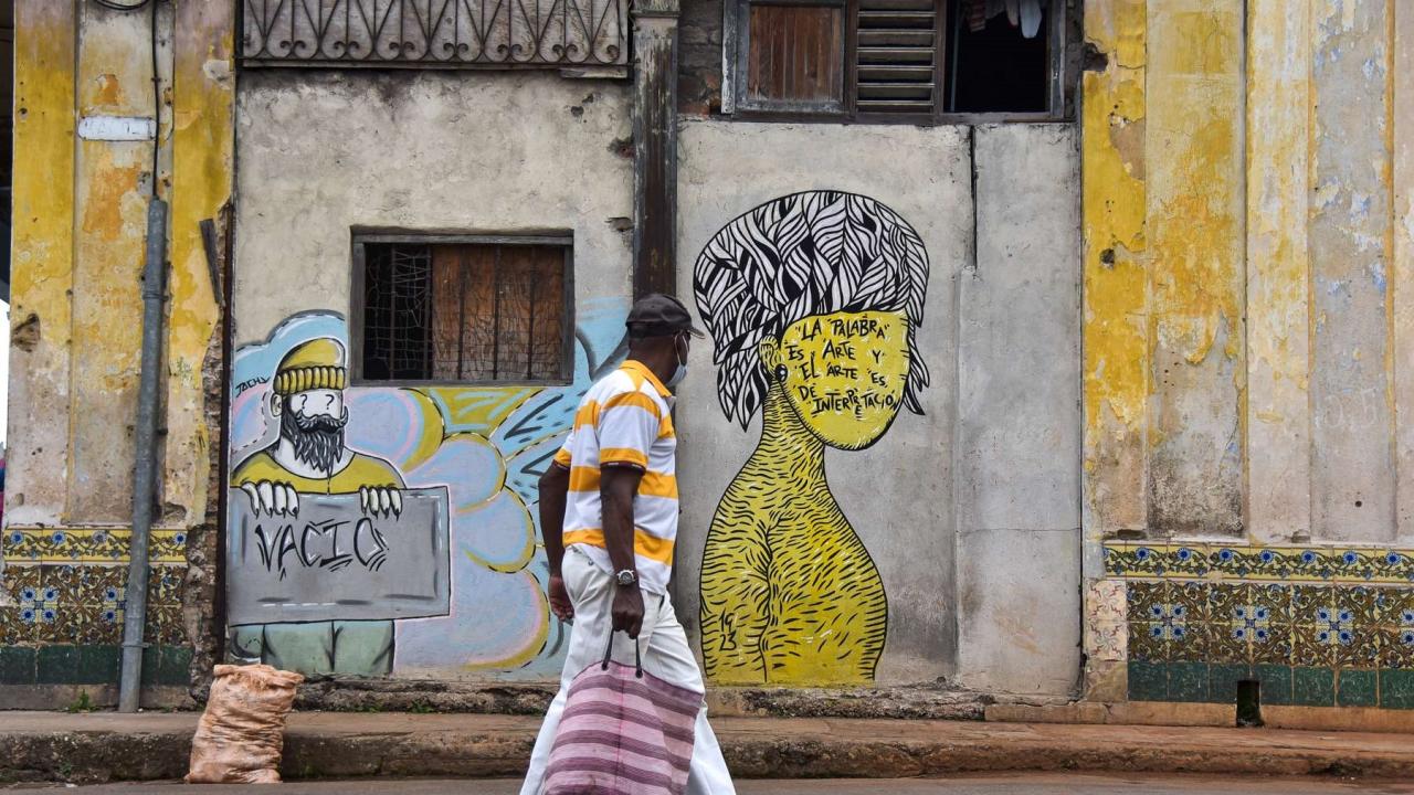 Un hombre cruza ante dos grafitis en una calle de La Habana.