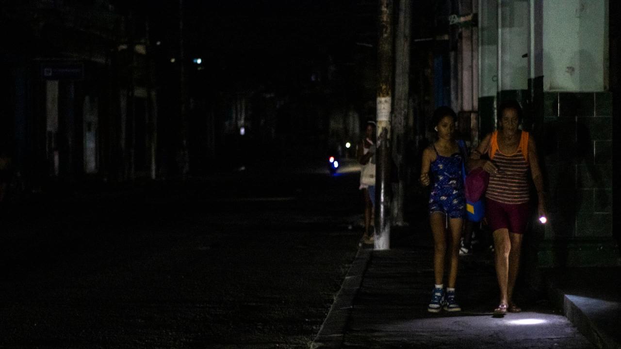 Dos cubanas por la acera de una calle a oscuras.