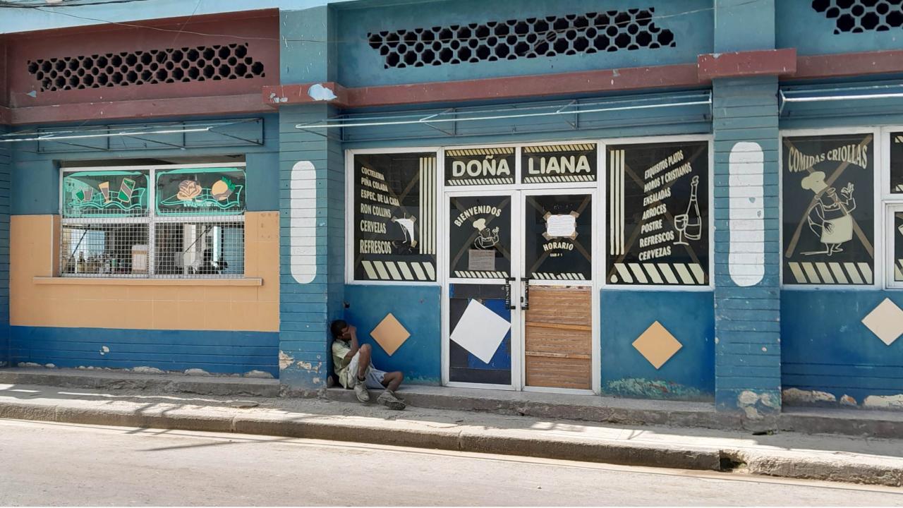 Un cubano sentado a la entrada de un comercio cerrado.