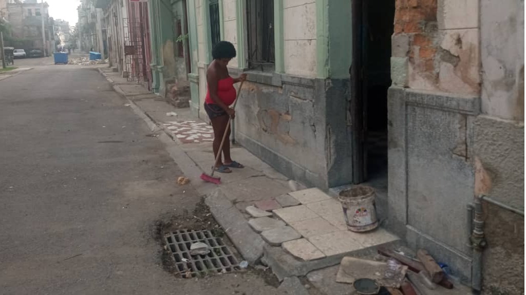 Una mujer embarazada barre el frente de una vivienda en La Habana.