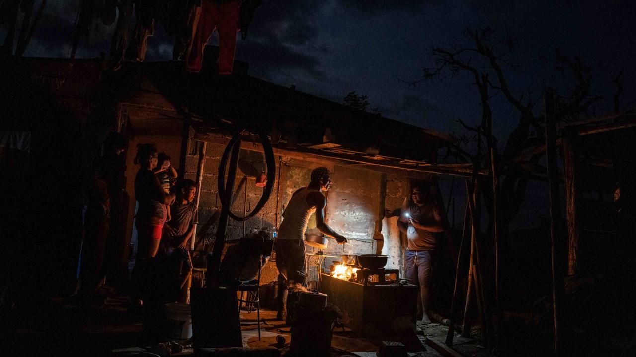 Cubanos cocinando con leña a la luz de la linterna de un teléfono.