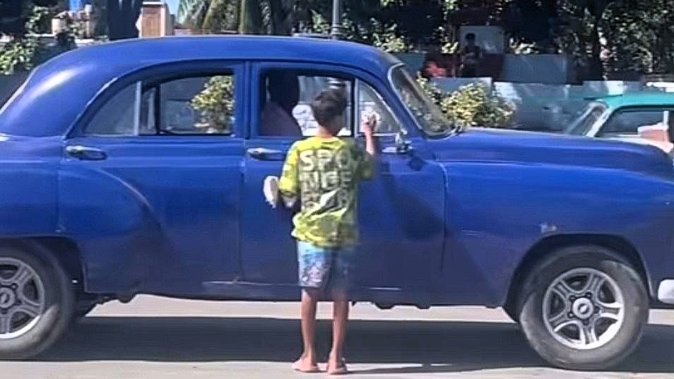 Un niño en La Habana limpia cristales a un coche con la esperanza de ganar dinero.