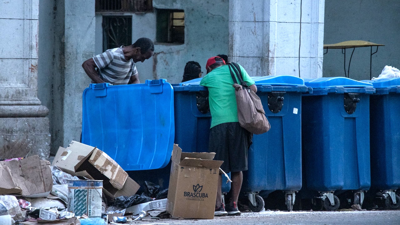 Dos hombres buscando sustento en un contenedor de basura.