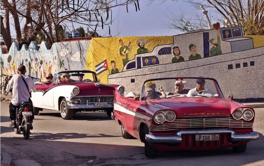 Turistas pasean en autos clásicos frente a un mural, en La Habana.