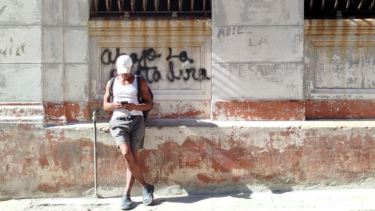 Un hombre recostado sobre una pared con una pintada contra el régimen.