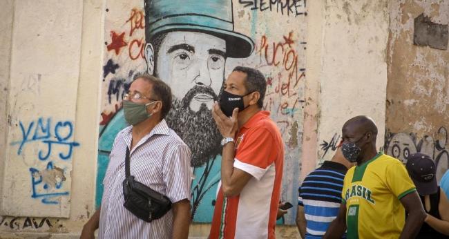 Cubanos pasan por delante de una pintura con el rostro de Fidel Castro.