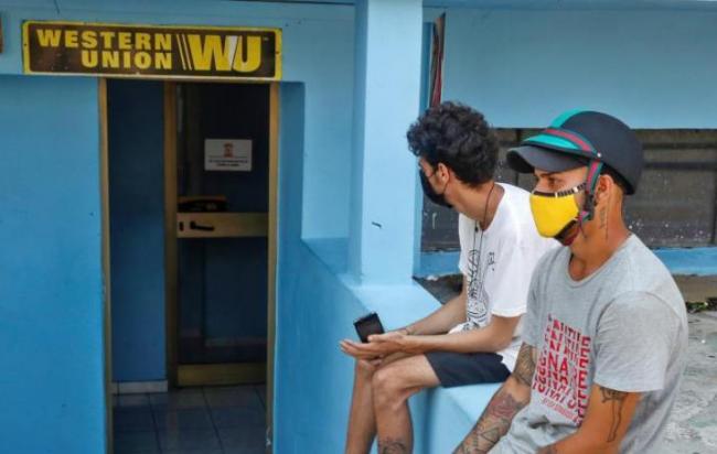 Dos jóvenes cubanos esperan fuera de una oficina de Western Union.