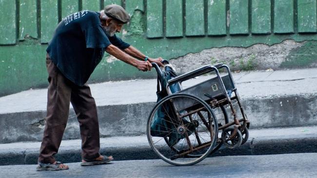 Un anciano cubano empuja su silla de ruedas en una loma.