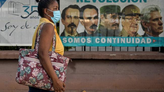 Una mujer camina delante de un cartel en La Habana.