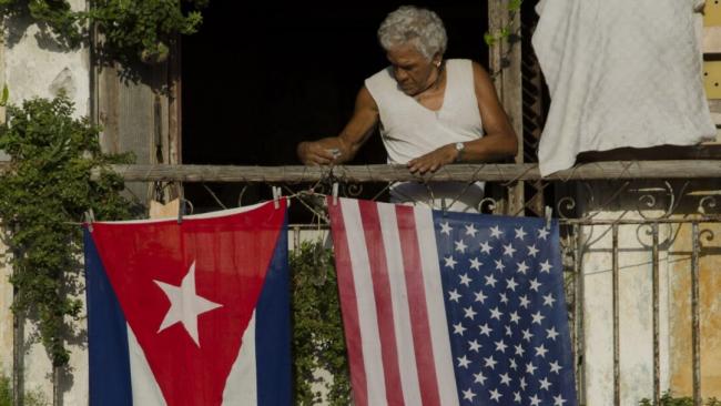 Una mujer en un balcón de la Isla con las banderas de Cuba y EEUU. 
