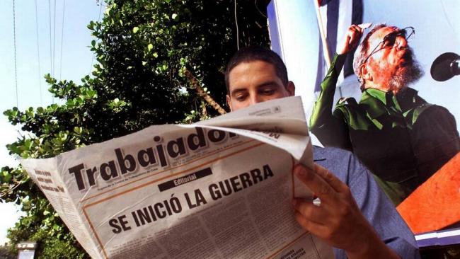 Un cubano con el periódico Trabajadores, ante una pancarta de Fidel Castro.