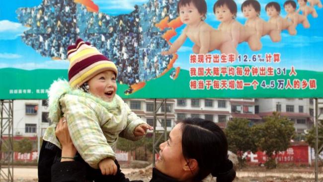 Una mujer china levanta a su hijo frente a una valla de propaganda de planificación familiar en el condado de Xinshao.
