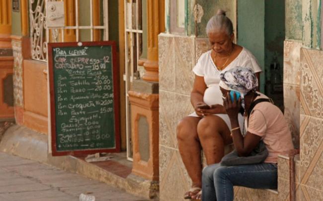 Dos mujeres cubanas se comunican por teléfono en la puerta de una vivienda en La Habana.