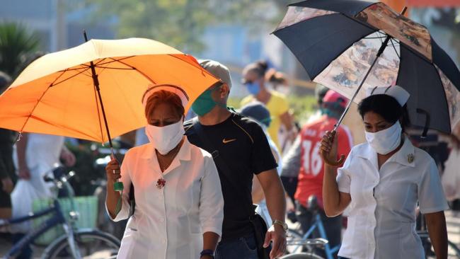 Cubanas protegiéndose del sol con sombrillas.
